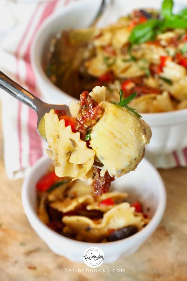Forkful of Italian Pasta Salad with bowtie pasta, basil, artichoke heart and sun-dried tomato on fork.