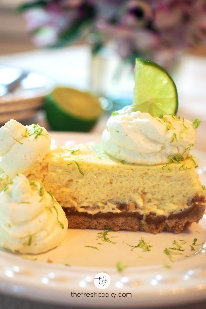 side view of key lime torte on a plate with whipped cream dollops and lime zest.