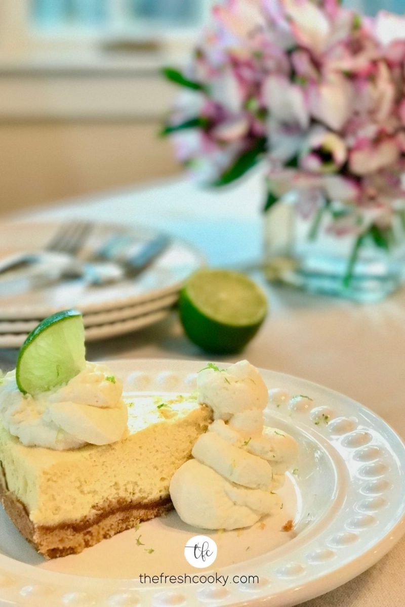 wedge of key lime torte on a plate with flowers in background and plates ready for serving.