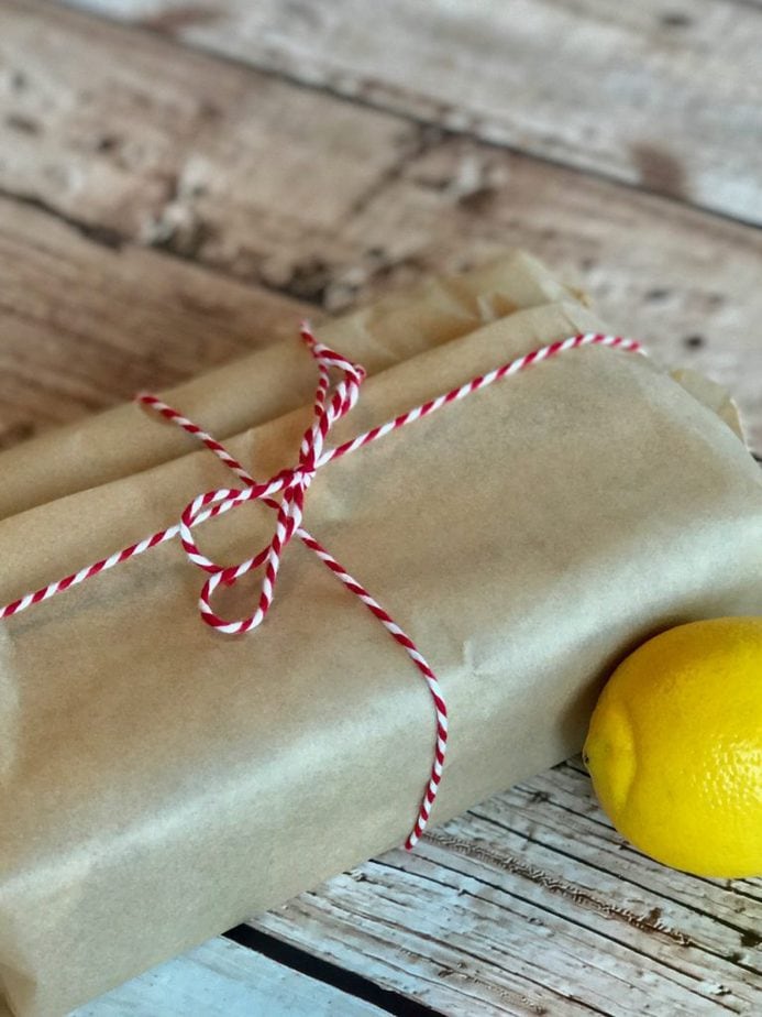 A loaf of lemon zucchini bread wrapped in natural parchment paper tied with red and white bakers twine.