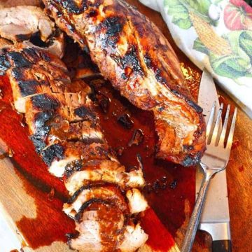 two tenderloins of asian marinated grilled pork tenderloin on a cutting board with sauce, carving knife and fork