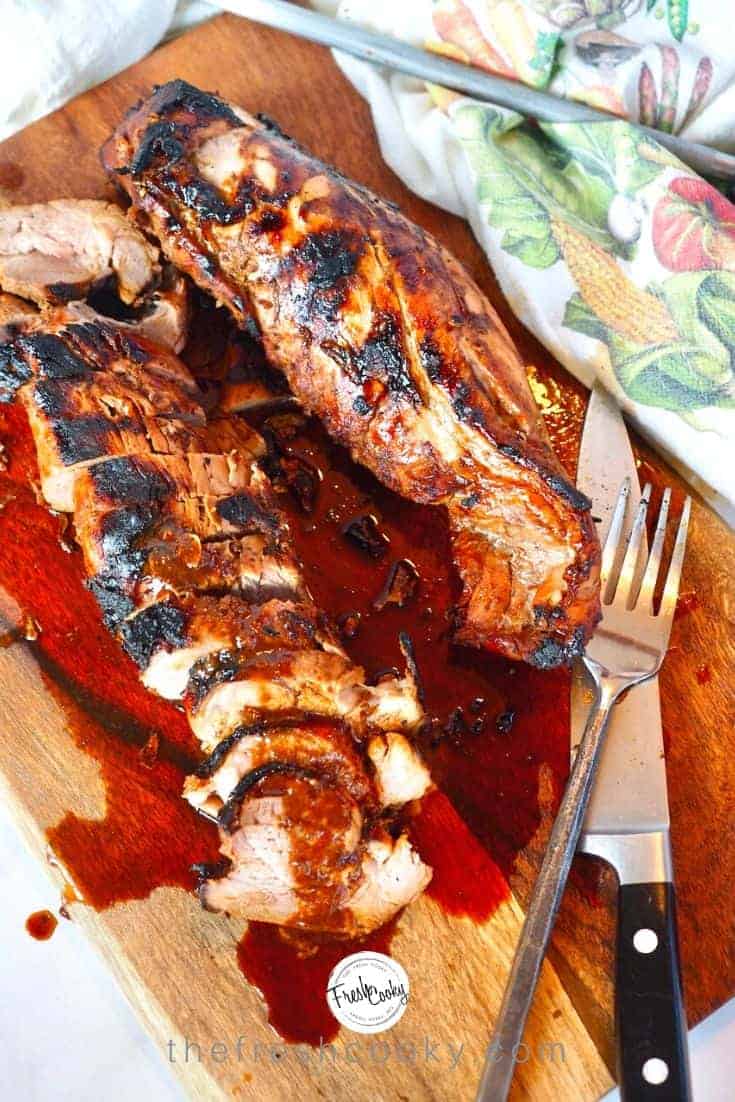 two tenderloins of asian marinated grilled pork tenderloin on a cutting board with sauce, carving knife and fork