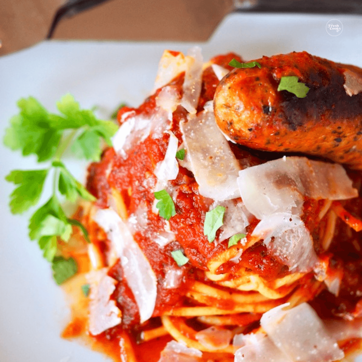 Easy Authentic Italian Spaghetti Sauce on a plate, topped with shaved parmesan and a piece of sausage. 