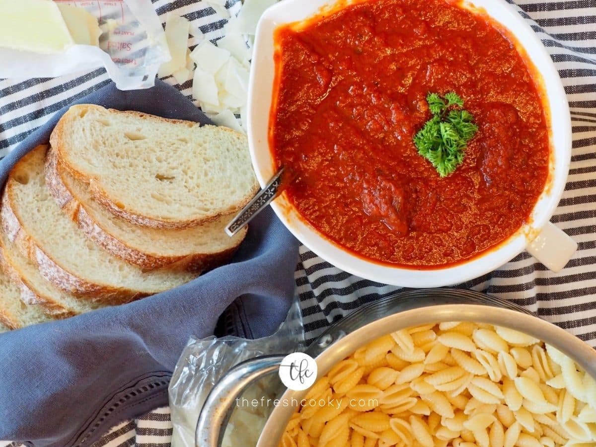 Bowl of spaghetti sauce with cooked pasts and bread nearby.