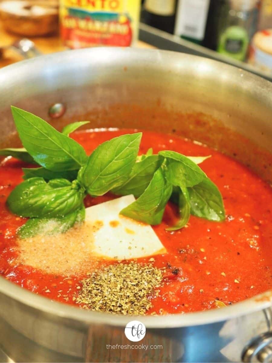 Large pot filled with tomatoes, fresh basil, parmesan rind, spices, herbs.