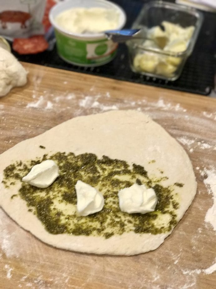 rolled out pizza dough with pesto spread on one half and dollops of ricotta cheese for easy calzones