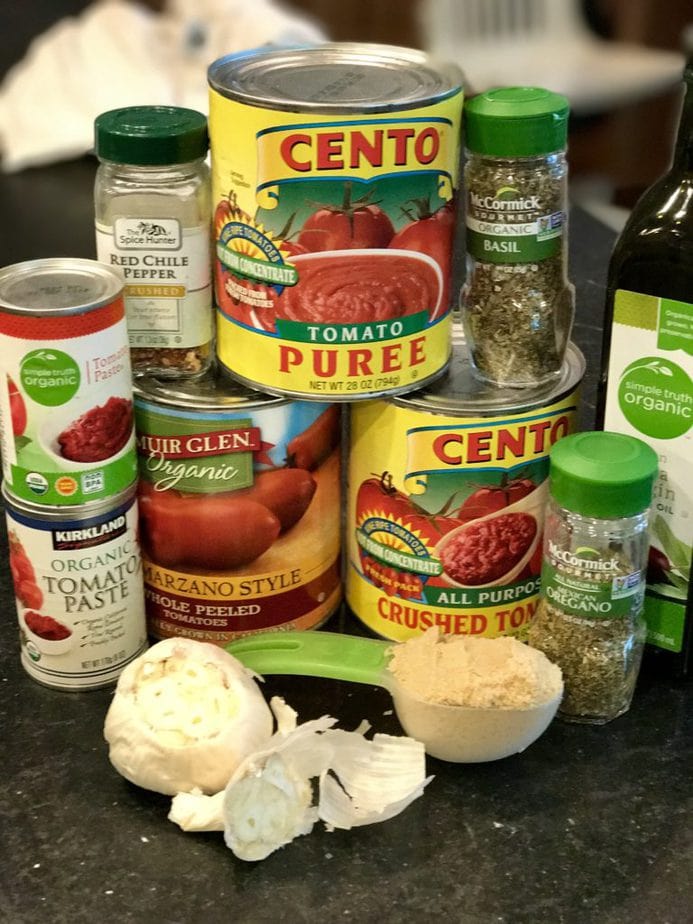 Ingredients pictured for spaghetti sauce. San Marzano tomatoes, tomato puree, crushed tomatoes, garlic, brown sugar, tomato paste, olive oil, dried basil, dried oregano and red pepper flakes. 