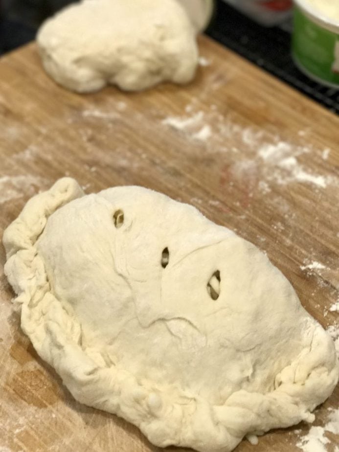 Easy Calzone on a cutting board ready for the oven, pinched edges and 3 slits cut into the top of the pizza pie. 