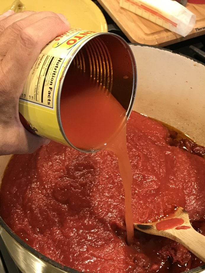 Water rinsed out cans of tomatoes and pouring into the sauce ingredients. 