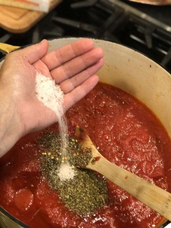 handful of kosher salt going into pot of spaghetti sauce ingredients. 
