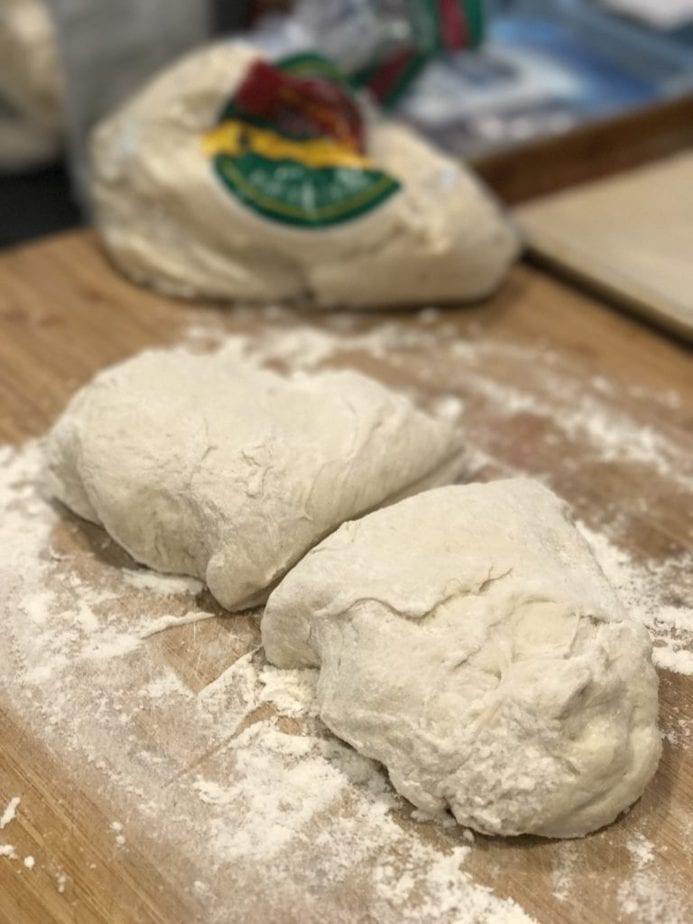 Image of pizza dough, on cutting board with flour and cut in half ready to roll for easy calzones