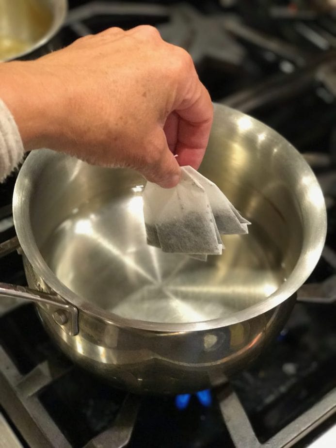 Hand adding tea bags to simmering water on stove for Chai Tea Latte