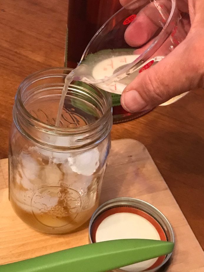 Pouring from a mini measuring cup, fresh lemon juice into mason jar with ice