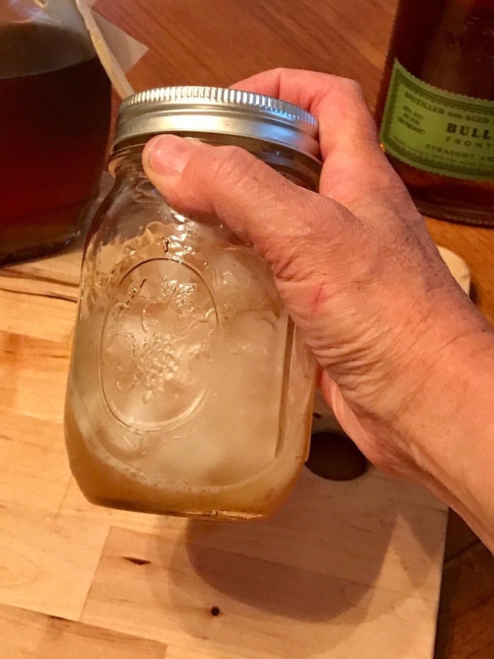 Hand holding a mason jar filled with maple whiskey sour and ice, shaking