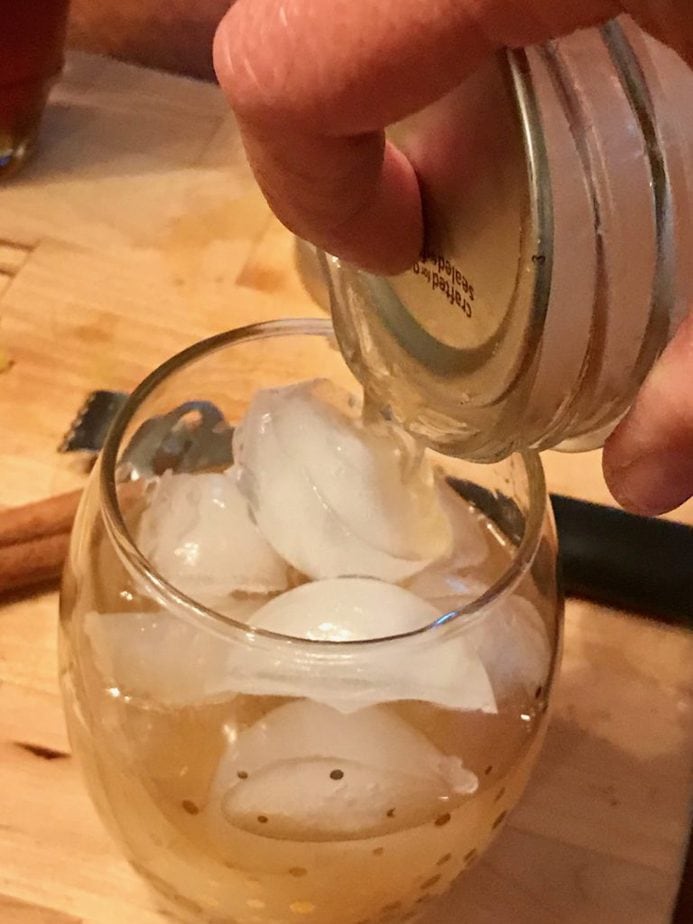 Image of hand pouring through strainer a maple whiskey sour that has been shaken into a shaped cocktail glass