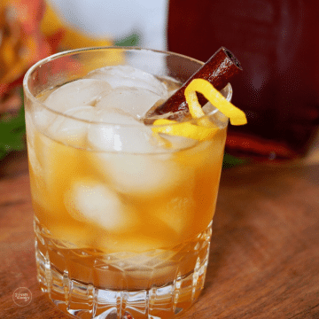 Maple whiskey sour in glass with cinnamon stick and lemon zest.