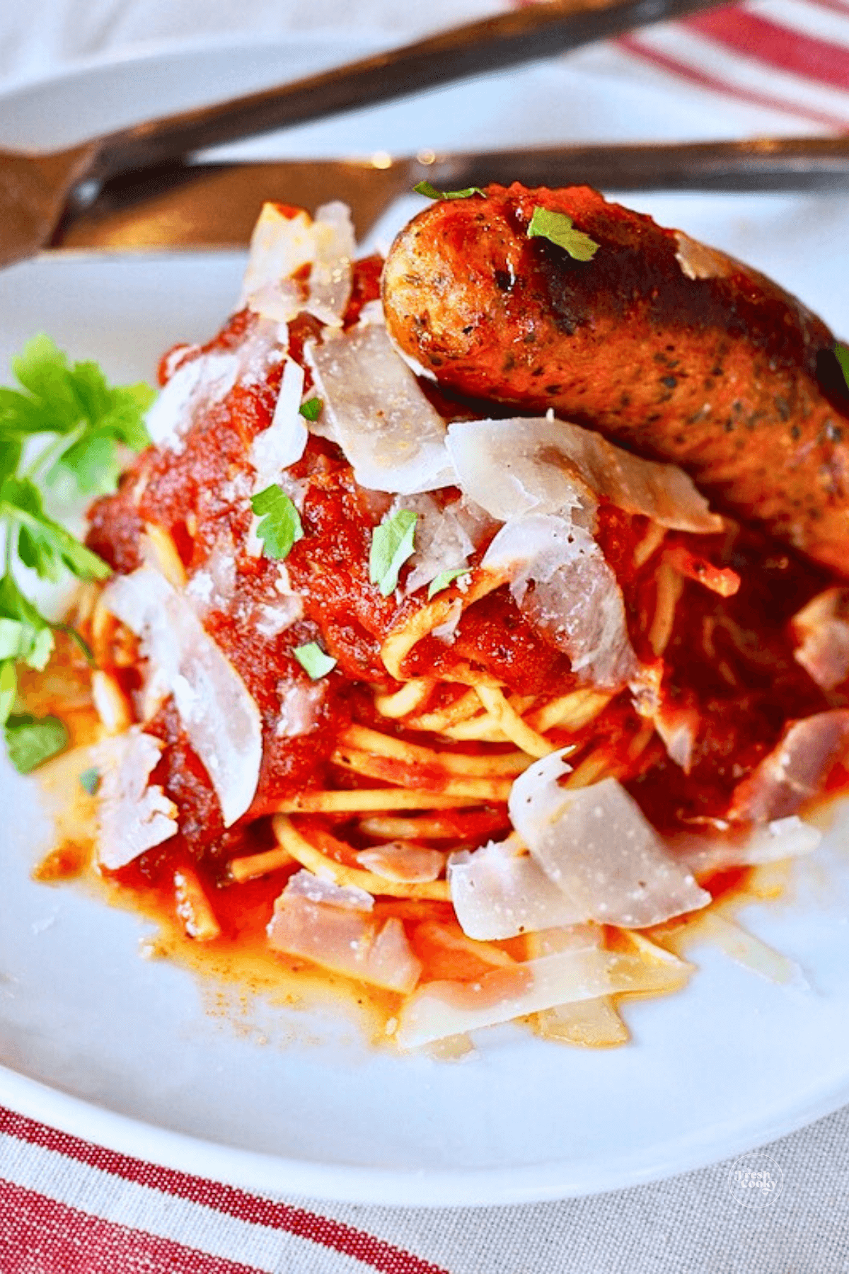 Plate of spaghetti swirled with rich Italian spaghetti sauce and topped with shaved parmesan and a sausage.