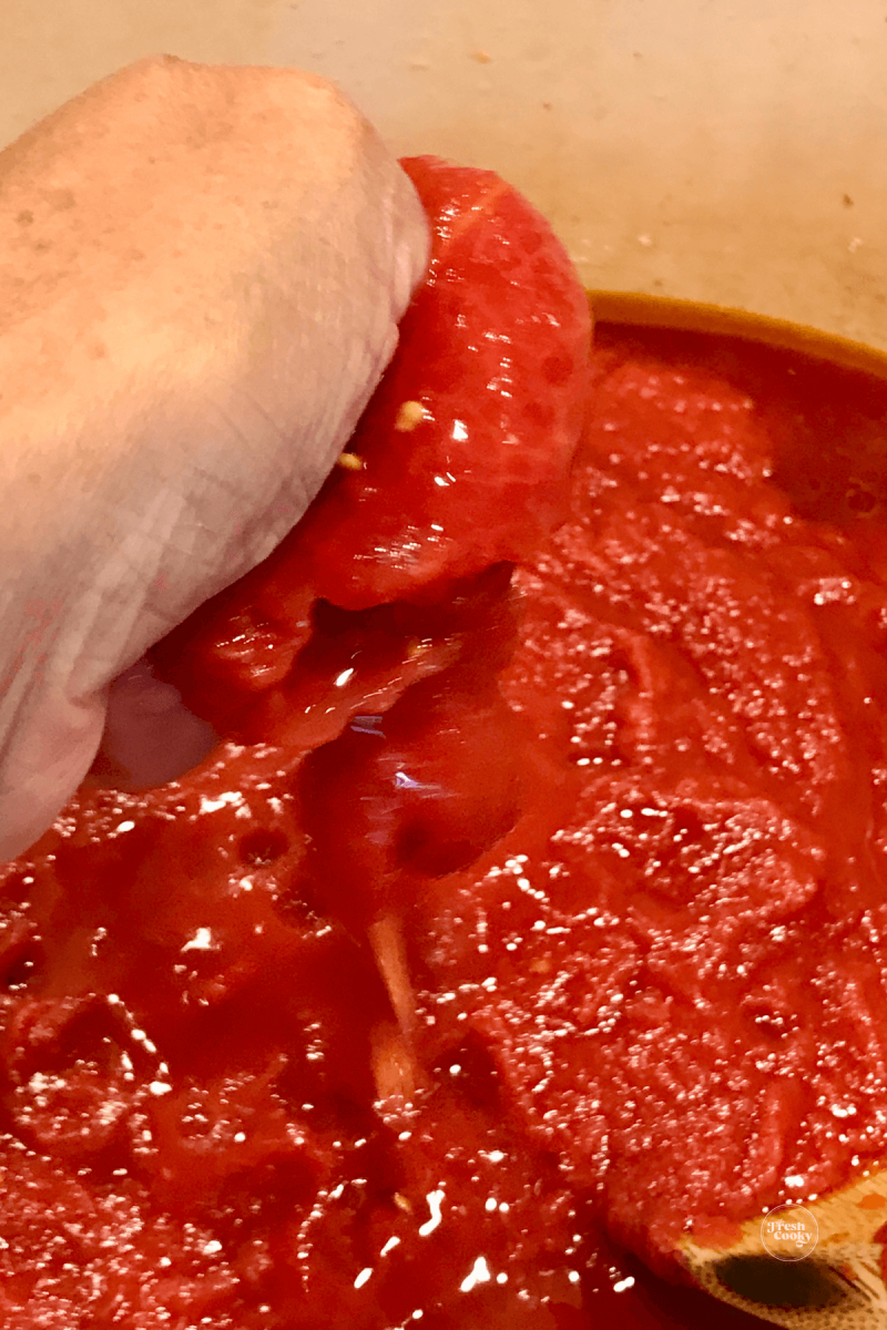 Hand squeezing whole tomatoes into sauce.