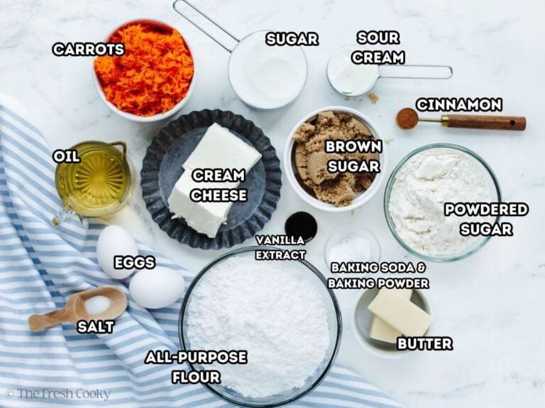 Labeled ingredients for carrot cupcakes and frosting, L-R Oil, shredded carrots, sugar, sour cream, cinnamon, powdered sugar, butter, baking soda, baking powder, vanilla, brown sugar, all-purpose flour, cream cheese, eggs, salt.