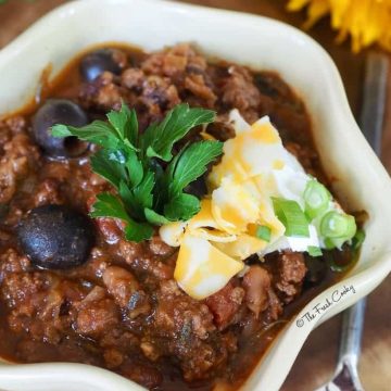 bowl of firecracker chili with shredded cheese, parsley and black olives