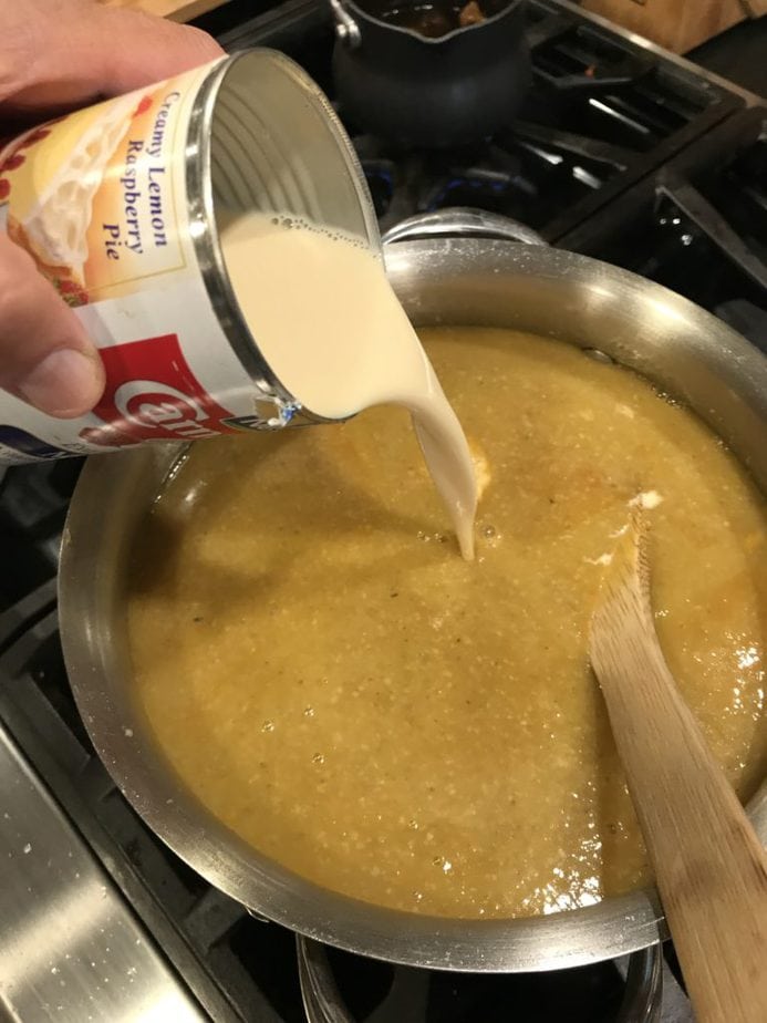 Pouring in evaporated milk into saucepan with pumpkin soup. Wooden spoon on side.