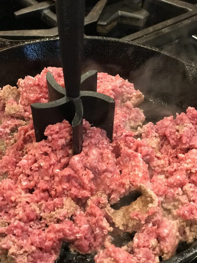 chopping ground beef in cast iron skillet.