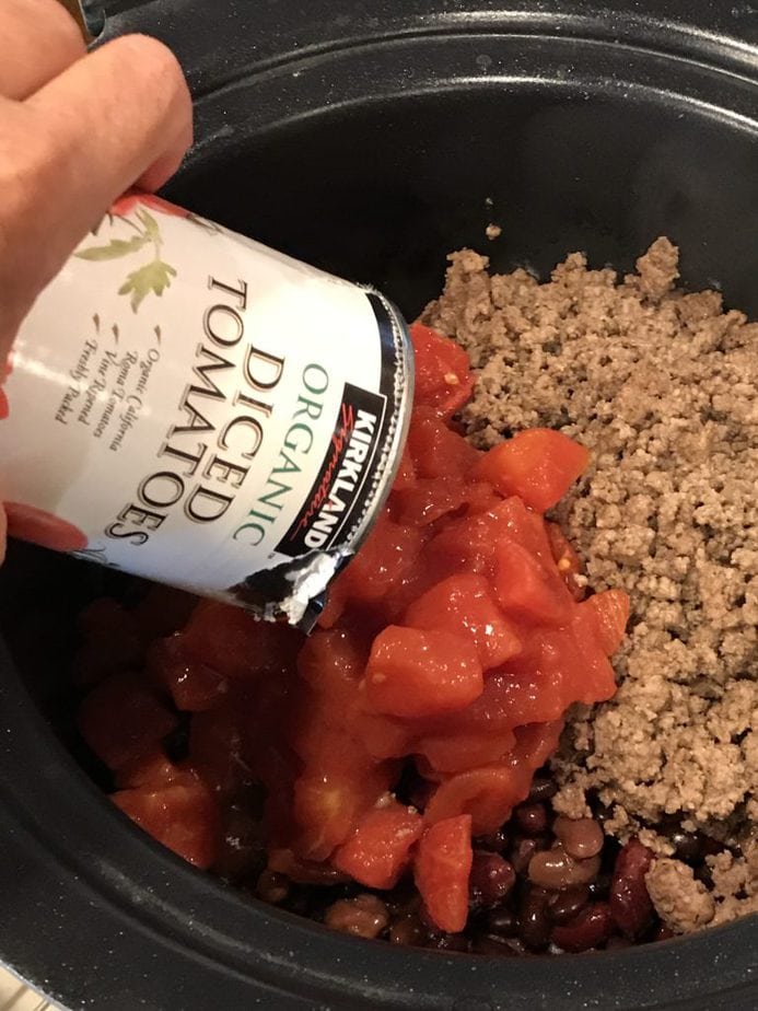 ADDING DICED TOMATOES TO GROUND BEEF mixture in crockpot for firecracker chili.