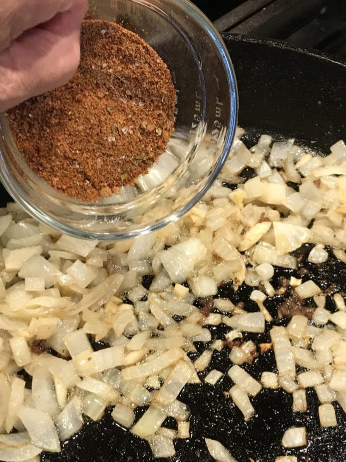 Pouring spices into saute pan with softened onions and garlic to bloom the spices for chili with zucchini.