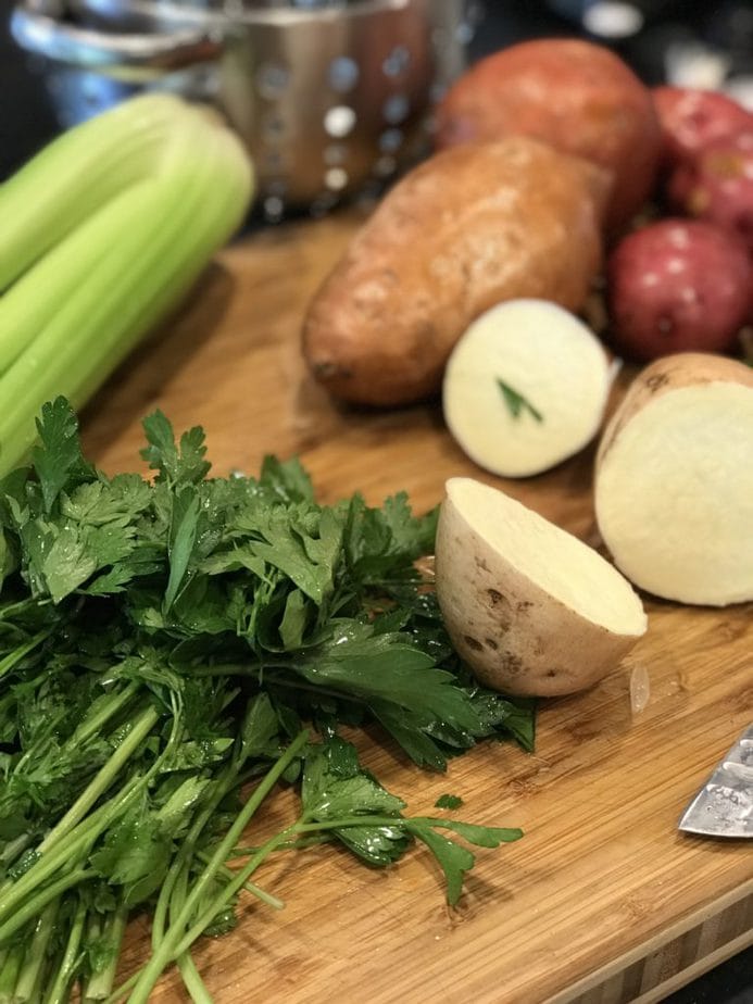 cutting board with parsley, celery, chopped potatoes and washed sweet potatoes and red potato in the background.