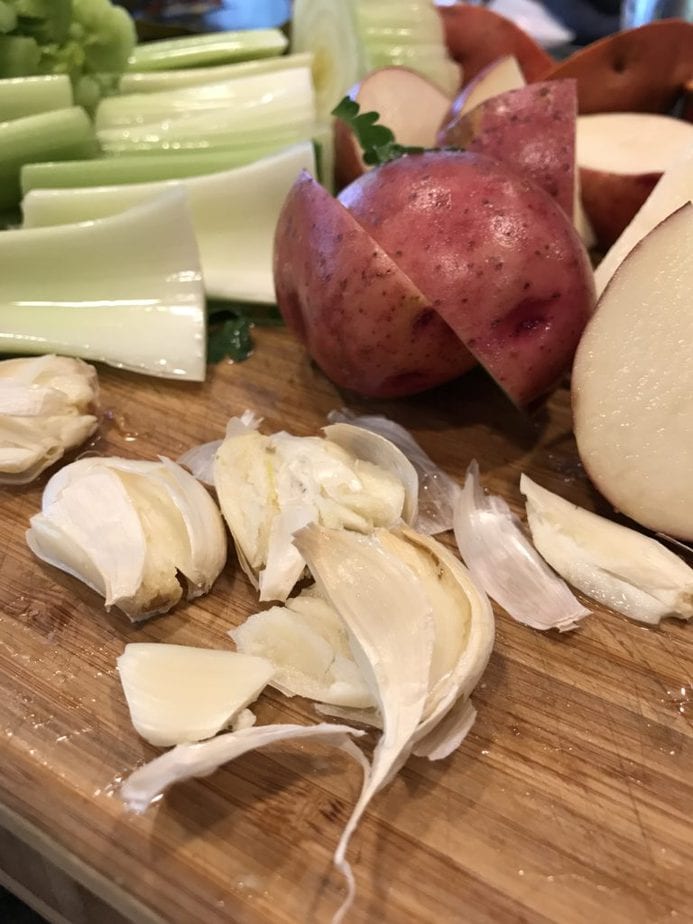 Chopped celery, halved red potatoes, garlic cloves smashed in foreground.