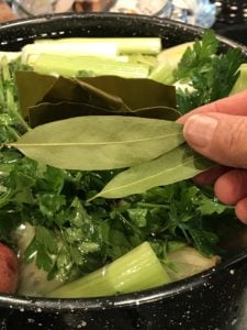 large pot filled with lots of chopped veggies, hand holding 2 bay leaves