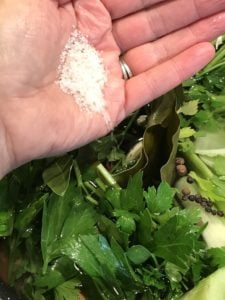 hand with sea salt in palm, pouring into large pot 