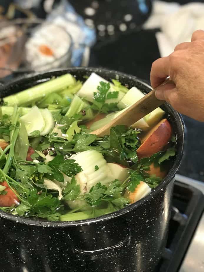 Stirring large black pot of veggies with wooden spoon.