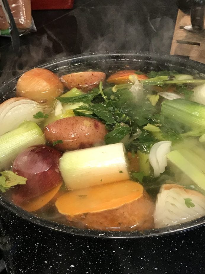 Large black pot of boiling water with rough chopped veggies, celery, onions, parsley, potatoes.