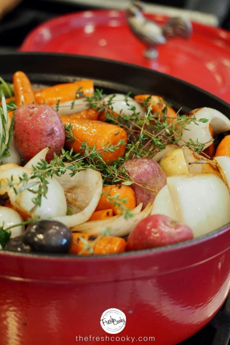 Dutch oven filled with carrots, onions, potatoes, pot roast and broth ready to go in the oven.