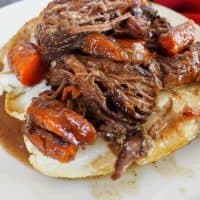 pot roast stuffed potato on a white plate with roast and carrots around.