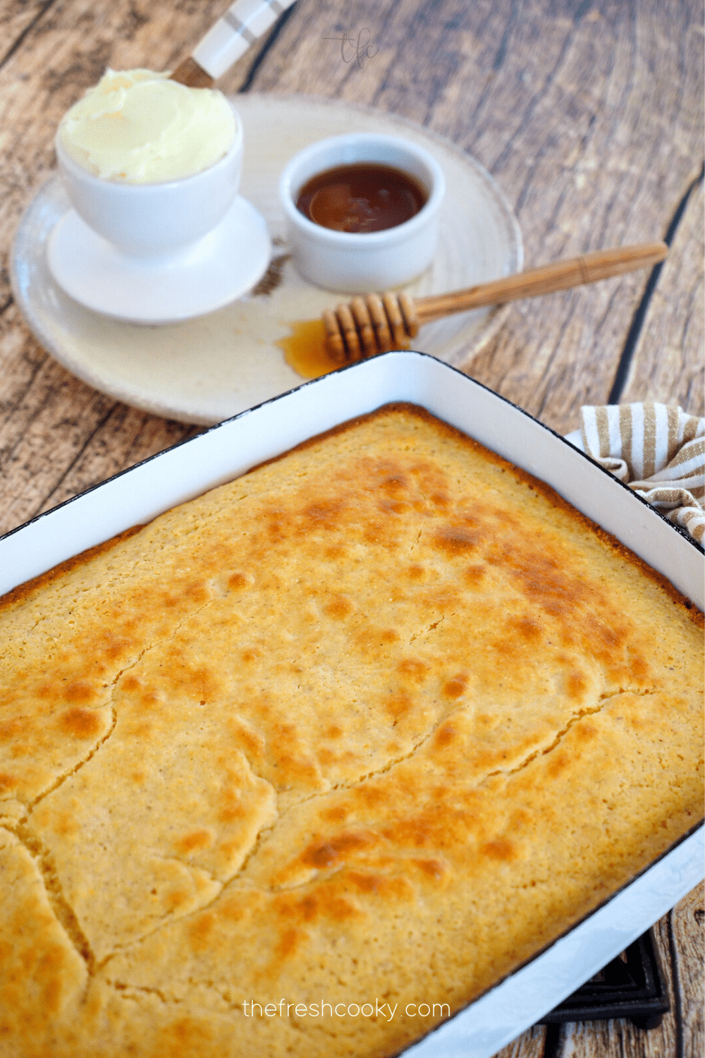 Best sweet cornbread recipe in pan with butter and honey behind ready to cut.