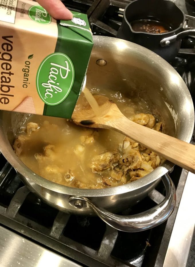 Pouring Pacific vegetable broth into saucepan with wooden spoon and mushrooms and onions.
