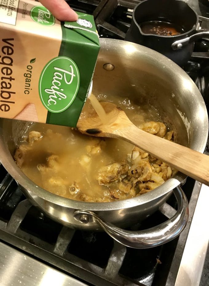 Pouring Pacific vegetable broth into saucepan with wooden spoon and mushrooms and onions. 