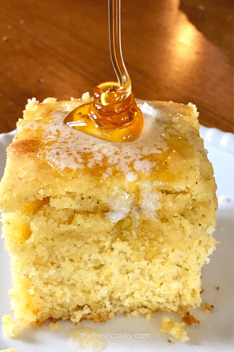 Image of square of sweet buttermilk cornbread on a plate with melting butter and a swirl of honey being pouring on top.