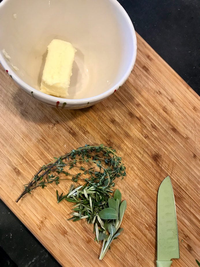 How to make herbed butter; herbs on cutting board with knife and stick of soft butter in small bowl to side. Tender Turkey | www.thefreshcooky.com