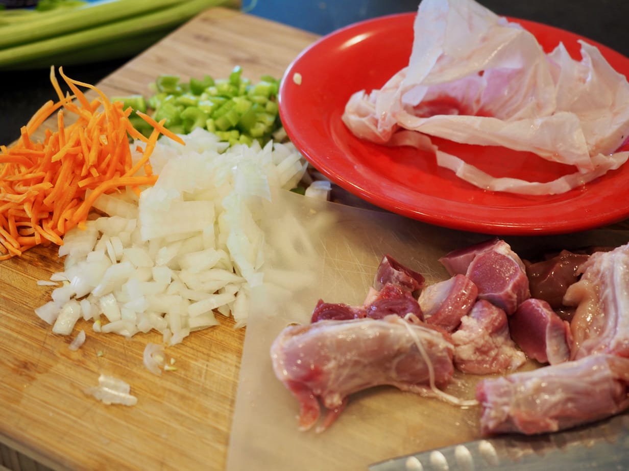 Raw turkey giblets on cutting board, chopped onions, celery and carrots in background; the backbone of Giblet Turkey Gravy. 
