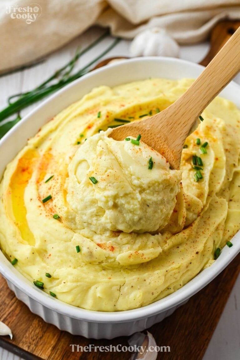 A white casserole dish filled with creamy garlic mashed potatoes with a spoon scooping a serving out, to pin.