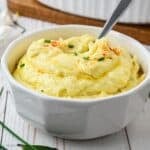 A pretty white scalloped bowl filled with creamy garlic mashed potatoes with a spoon.