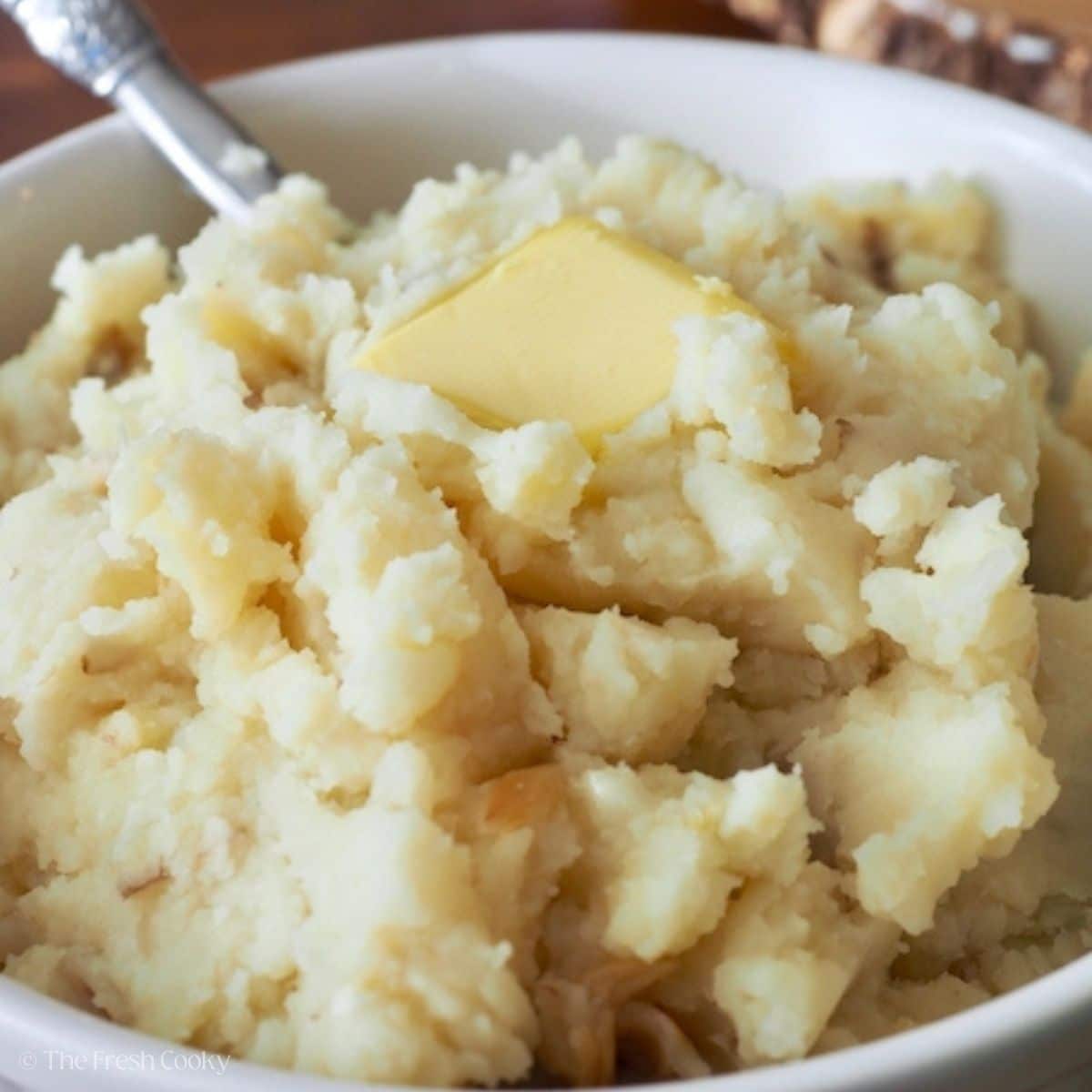 Bowl of garlic mashed potatoes with a slab of butter melting on top.