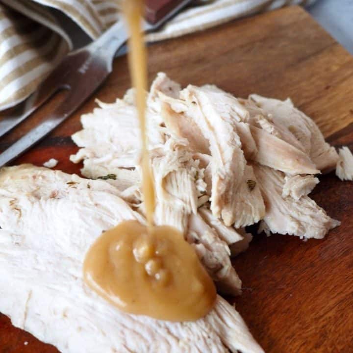 image of sliced turkey pouring giblet gravy on top sitting on a cutting board.