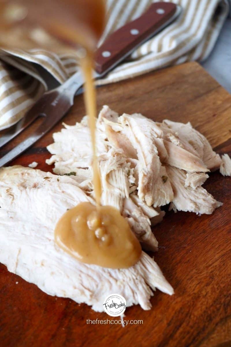 image of sliced turkey pouring giblet gravy on top sitting on a cutting board.