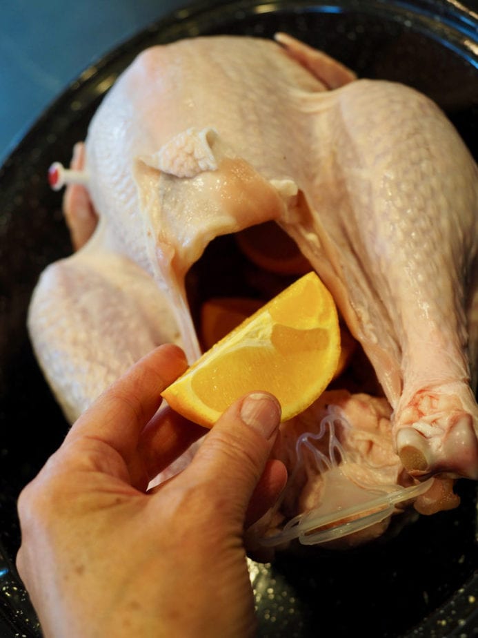 Hand holding orange wedge and placing inside turkey cavity. Tender Turkey | www.thefreshcooky.com