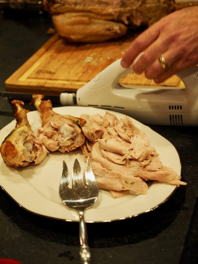 Using an electric knife to carve a roasted turkey, turkey sitting on cutting board, with platter near by. Carving a turkey | via @thefreshcooky