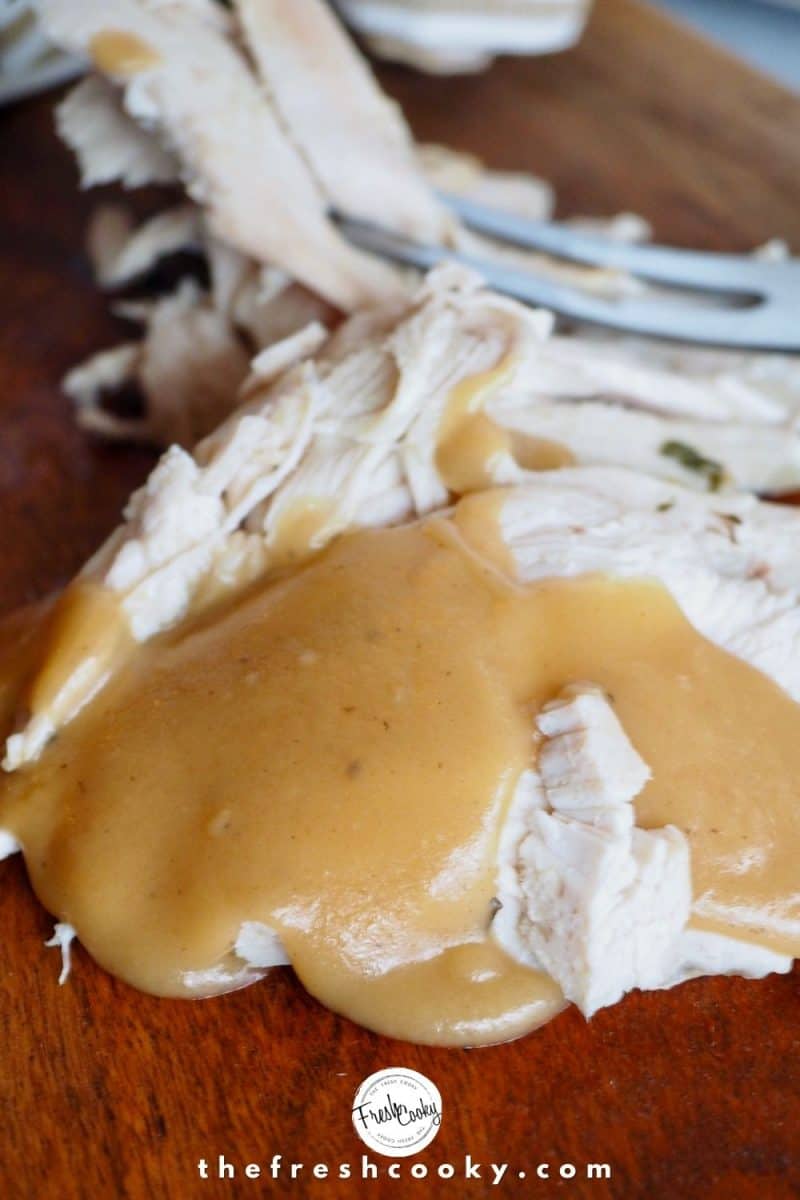 sliced roasted turkey breast on dark wood cutting board with a puddle of gravy on top.